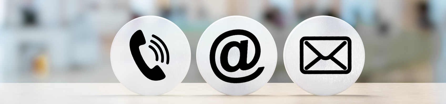 Contact Us. telephone, envelope letter and e-mail symbols on Wooden round in row on table with blurred office background, contact us symbols or web banner