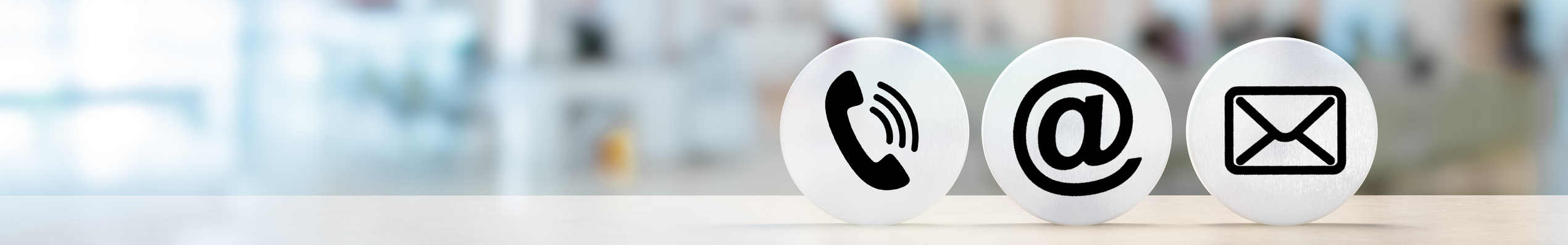 Contact Us. telephone, envelope letter and e-mail symbols on Wooden round in row on table with blurred office background, contact us symbols or web banner
